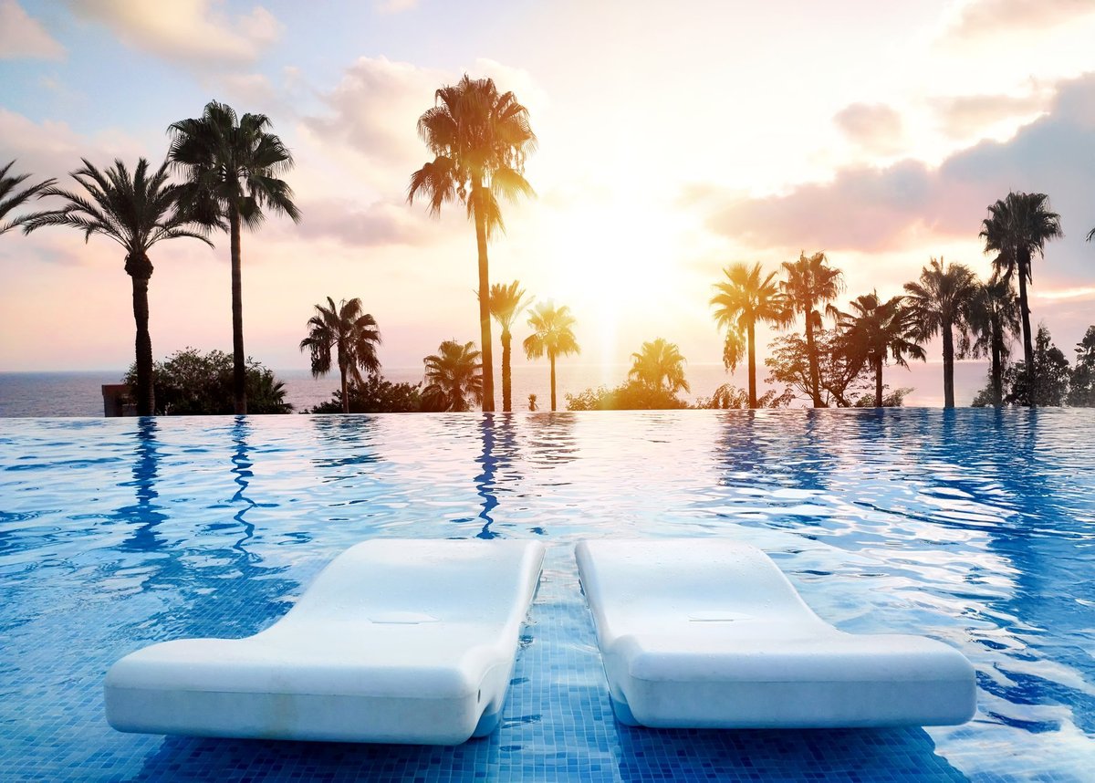 Golden-hour view across a tranquil landscaped pool area with palms and warm light